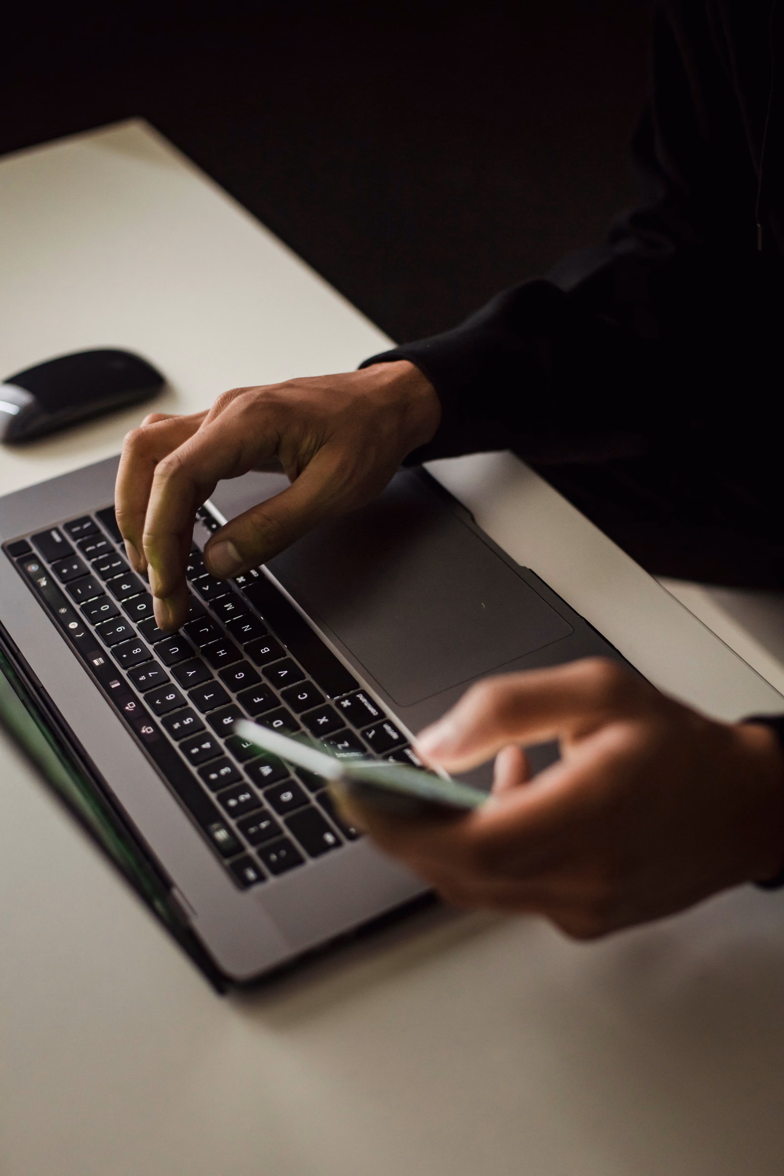 Person using a laptop and smartphone at the same time at a work desk