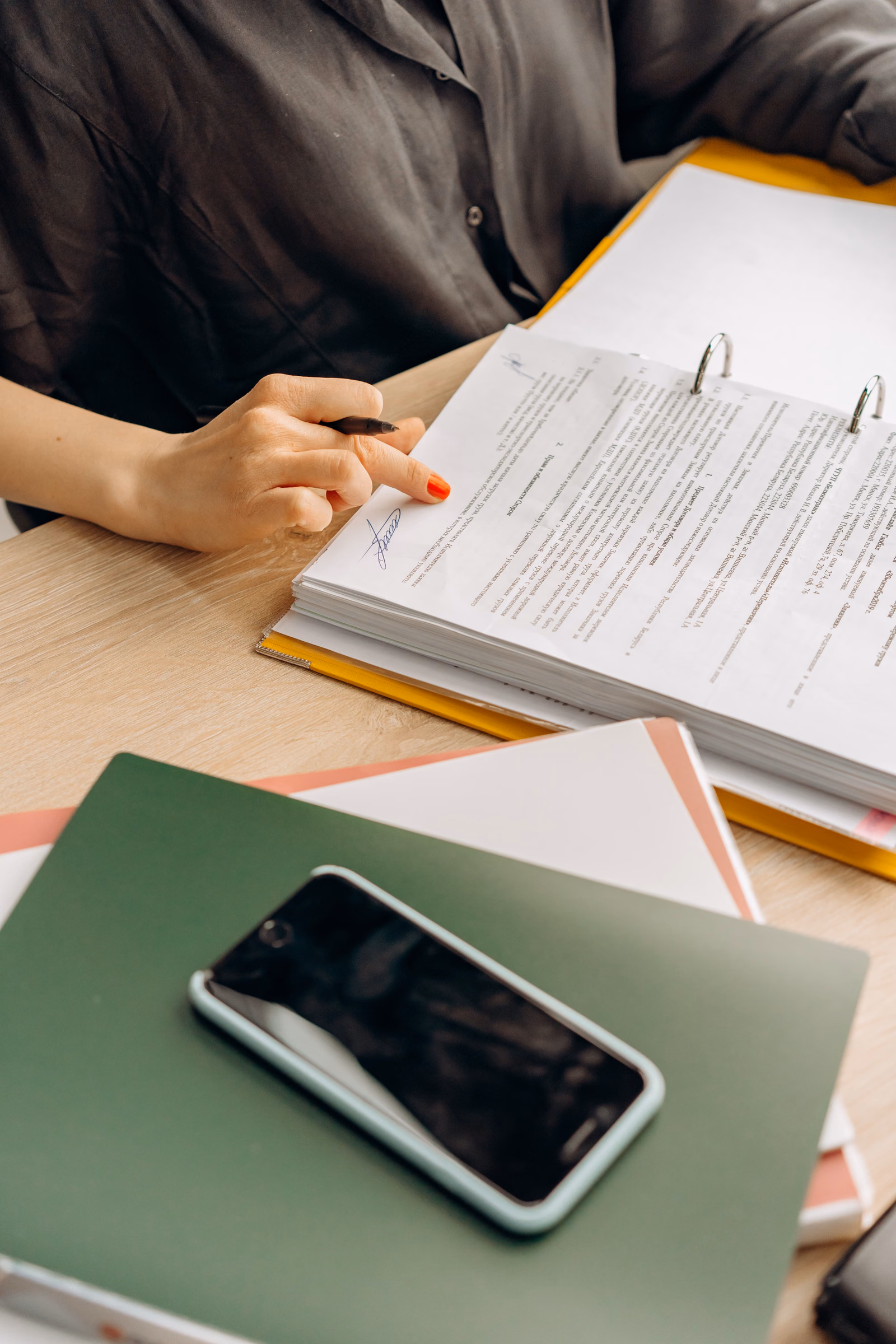 Person reviewing documents and files at a work desk with a smartphone
